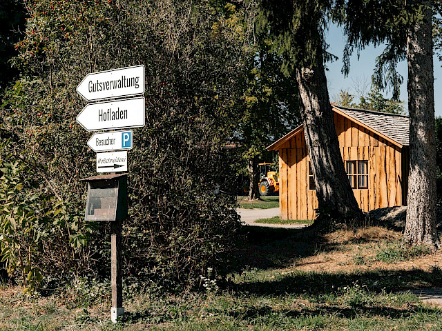 Wegweiser zu Hofladen und Gutsverwaltung neben einer Holzh&uuml;tte auf Gut Karlshof.