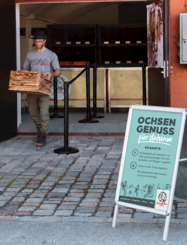 Ein Mann tr&auml;gt eine Holzkiste vor dem Hofladen auf Gut Karlshof.